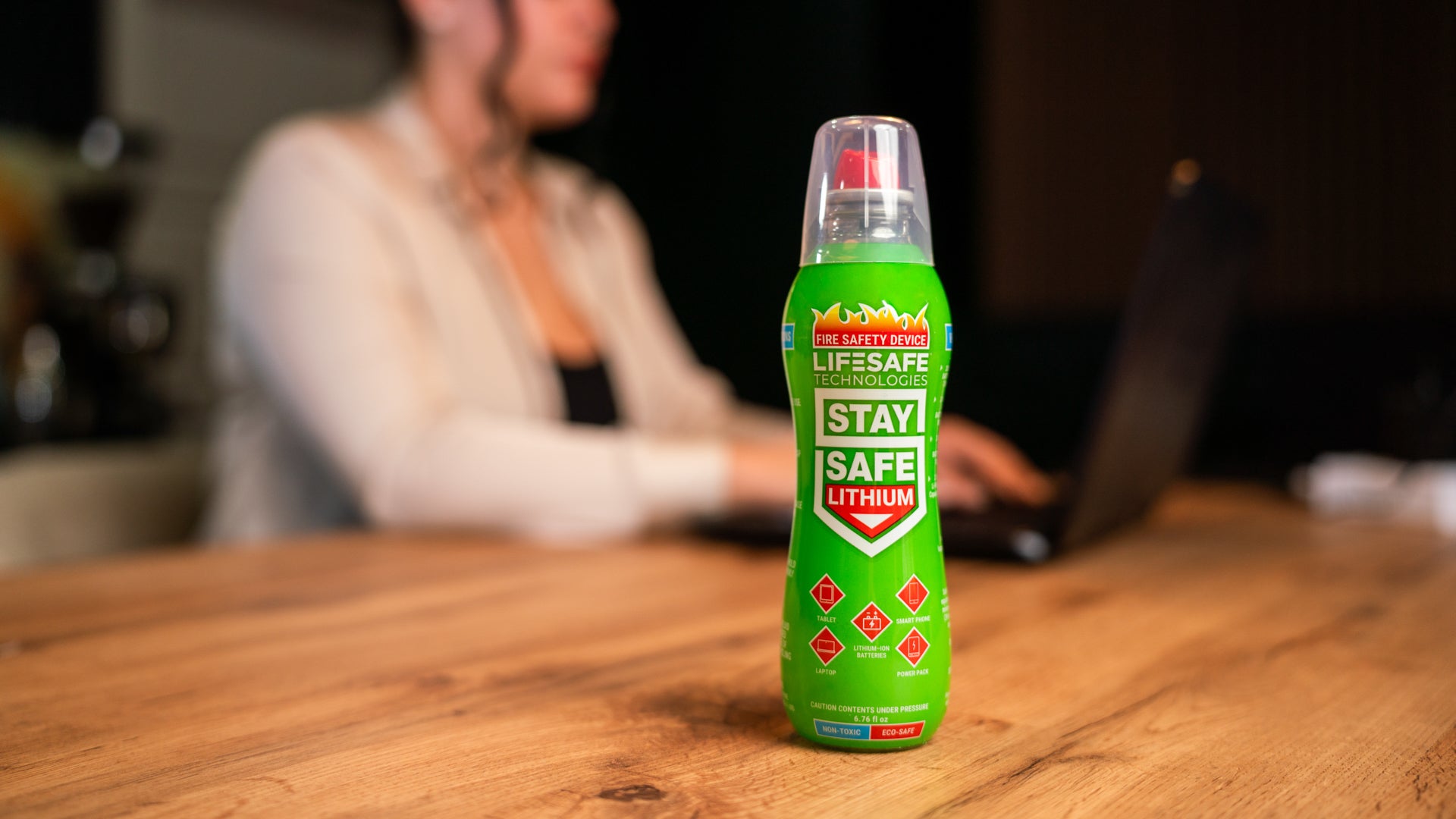 StaySafe Lithium bottle standing on a wooden table in a home environment with a person working on a laptop in the background