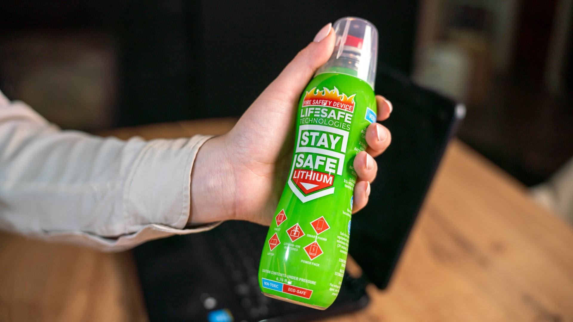 Hand holding the green StaySafe Lithium bottle next to a laptop on a wooden desk