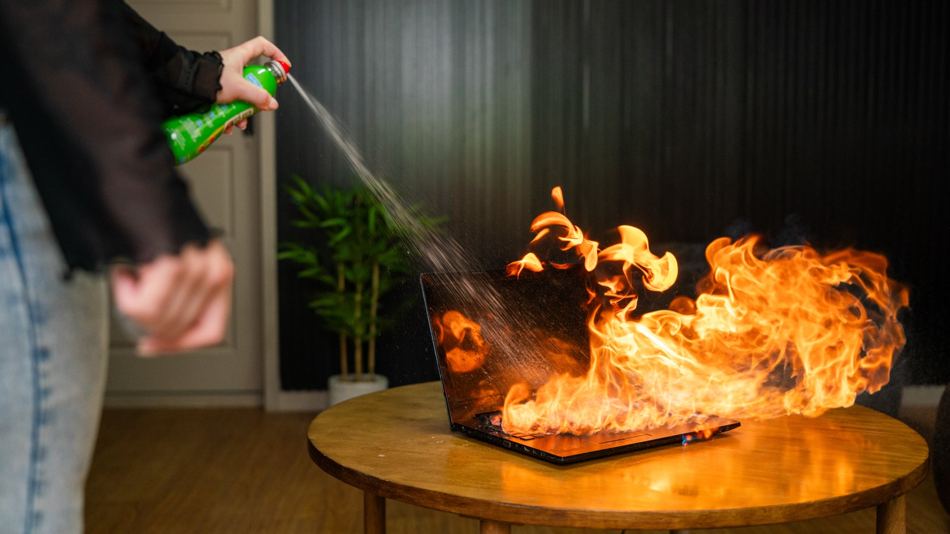 StaySafe Lithium fire safety device being sprayed onto a laptop engulfed in flames on a side table