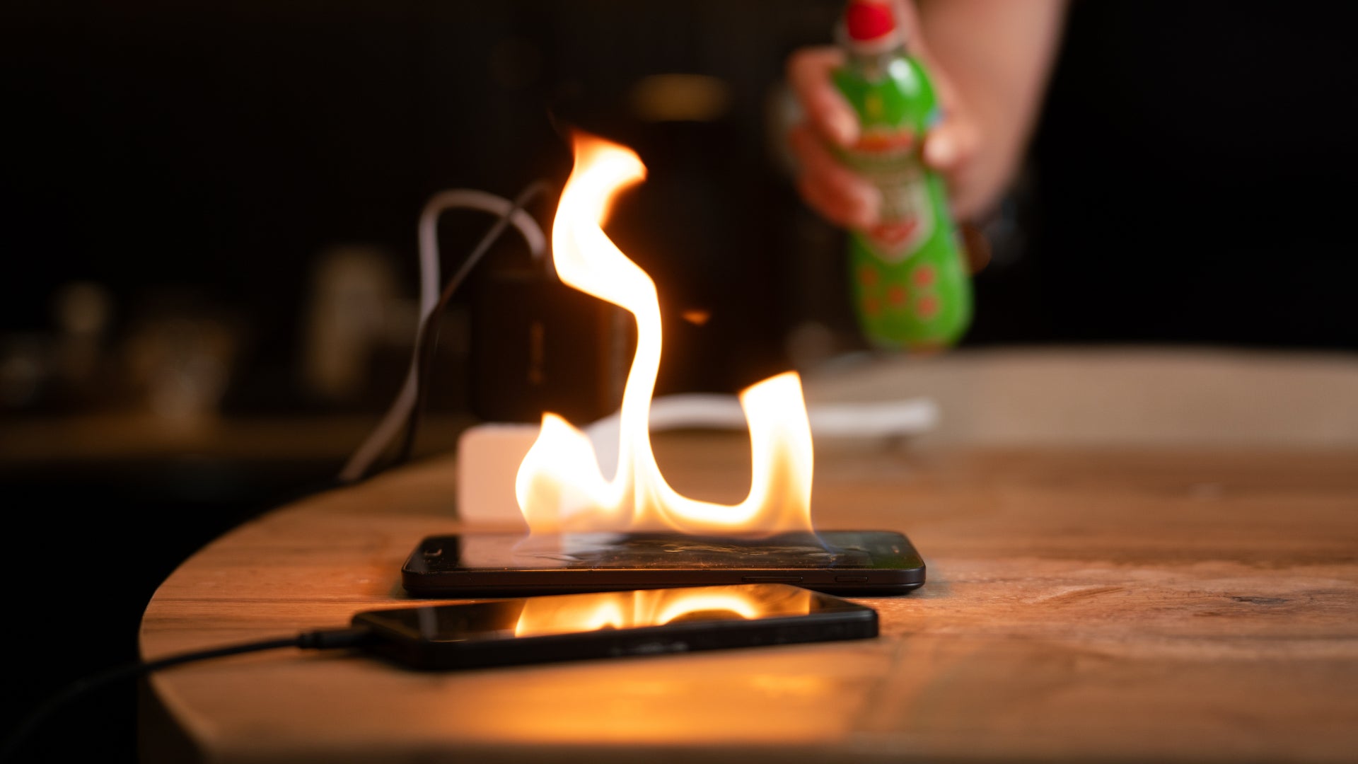 StaySafe Lithium being sprayed onto a phone and tablet on fire while charging on a wooden table
